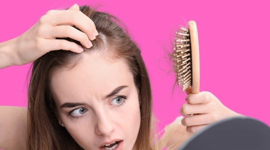 Woman checking hairbrush filled with hair and touching scalp